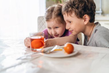 Paskalya için hazırlanıyorum. Komik çocuk ve kız masaya oturup yumurta boyarlar. Çocuklar yumurta rengini alana kadar bekler ve sürpriz ve zevkle renkleri seyrederler..