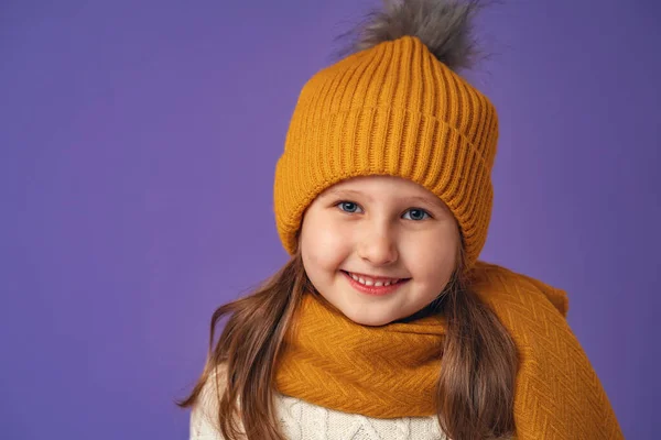 一个5岁的白人小女孩的画像 她的头发金黄 头戴黄帽 头戴围巾 站在紫色背景上开心地笑着 靠近点 — 图库照片