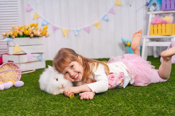 부활절 날귀여운 아기의 소녀가 색깔있는 달걀을 가지고 토끼에게 당근을 먹인다 — 스톡 사진