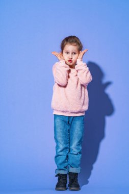 Şaşırmış çocuk kız ağzı açık bağırıyor ve mor arka planda izole edilmiş çılgın yüz ifadesi var. Şok olmuş küçük kız. Çocuk bağırıyor. Ellerini yüzüne doğru tutuyor.