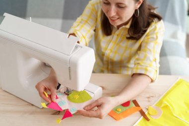 Gülümseyen mutlu kadın dikiş makinesinde keçeden çocuk uygulamaları dikmiş. Master yüksek sınıf yazar, dikiş hakkında blog tutar. Çocuk kıyafetleri ve tekstil uygulamaları.