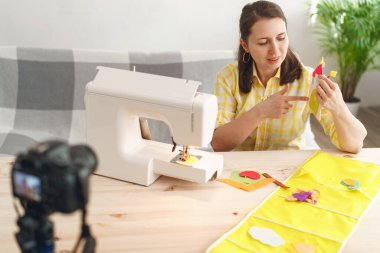 Mutlu gülümseyen kadın blogcu dikiş makinesine keçeden çocuk uygulamaları dikmiş. Master sınıfının yayını, dikiş hakkında bir blog işletiyor. Çocuk kıyafetleri ve tekstil uygulamaları.