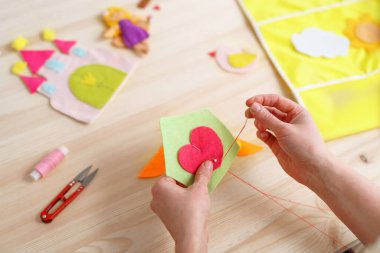 Kadınların elleri el işi yapıyor, keçeden yapılma bir ev dikiyorlar. Tahta masadaki dikiş işleri için aksesuarlar. Çocuklar ve yetişkinler için bahar ya da yaz işleri. Oda dekorasyonu için yaratıcı DIY