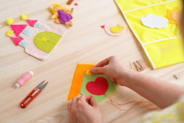 Kadınların elleri el işi yapıyor, keçeden yapılma bir ev dikiyorlar. Tahta masadaki dikiş işleri için aksesuarlar. Çocuklar ve yetişkinler için bahar ya da yaz işleri. Oda dekorasyonu için yaratıcı DIY