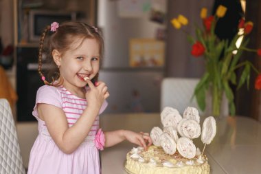 Sabahları mutfakta kremalı pasta yiyen tatlı küçük bir kız. Çocuk pastadaki kremayı parmağıyla deniyor. Ev Tatili