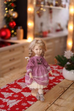 Eski moda tekstil el yapımı, insan yüzlü bir oyuncak bebek dekore edilmiş mutfaktaki masanın üzerinde duruyor. Tatil için oyuncak bebek yapıyorlar. Özel bir hediye. Dost Bebek!