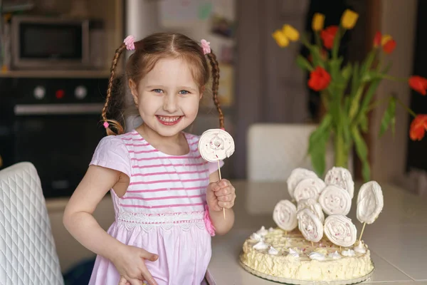 可爱的小女孩早上在厨房里吃奶油和蛋白饼 那孩子拿着糖果高兴极了 手里拿着糖果 家庭假期 — 图库照片