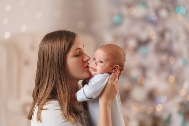 Mutlu, sevgi dolu genç bir anne küçük çocuğunu kollarına alır, ona sarılır ve öper. Kadın gülümsüyor, bebekle konuşuyor ve ona bakıyor. Annelik kavramı. Yakın plan.