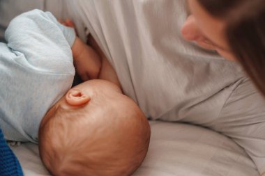 Mutlu genç kadın anne sütüyle besleniyor ve bebeğe sarılıyor. Bir anne yeni doğmuş bir bebeği yatakta yatarken emziriyor. Yeni doğan emzirme kavramı. Çocuk yatmadan önce süt içer. Yan görünüm.