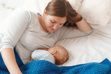 Mutlu genç kadın anne sütüyle besleniyor ve bebeğe sarılıyor. Bir anne yeni doğmuş bir bebeği yatakta yatarken emziriyor. Yeni doğan emzirme kavramı. Çocuk yatmadan önce süt içer. Yan görünüm.