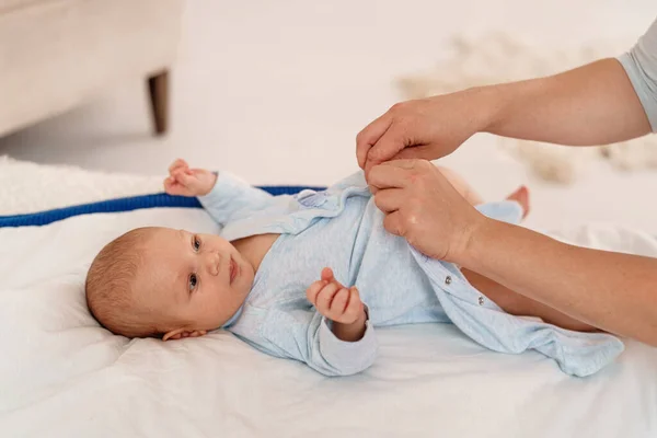 loving, caring mother changes clothes for a baby lying on his back on the bed. Daily care. Changes his diaper. The parent communicates with the child by talking and playing with him.