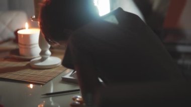 Aile akşamı mum ışığı ve fenerle. Çocuk kalemle çiziyor. Bir mum ışığında dalgalı saçlı bir çocuk yaratıcılıkla meşgul, çizim yapıyor..