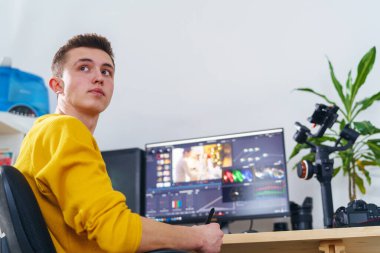 Yan görüş, erkek-kameraman kalem tableti ve özel bir program kullanarak evdeki bilgisayarın önünde video işleme yapıyor. Video düzenleme. Blog yazıyorum. Serbest çalışan biri. Uzaktan kumanda. Eğitim yeniden başlatılıyor