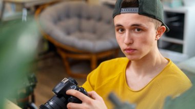 Genç bir fotoğrafçının portresi, kamerayı ayarlar, evdeki fotoğraf ve videoları gösterir. Genç adam fotoğraf ve videoları inceliyor. Program editöründe. Serbest çalışan biri. Uzak çalışma.