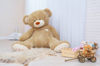 Dev oyuncak ayı, oyuncak sepetinde oyuncak, oyuncak ayılar, ahşap araba ve canavar yapraklarıyla dolu parlak bir odada oturuyor. Hafif tuğlalı duvarları ve ahşap parke döşemeleri olan modern bir iç mekan. Boşluğu kopyala