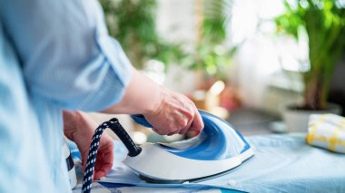 Yakın çekim, yan görüş, bir kadın ütüyü güneşli bir günde yıkadıktan sonra ütü masasının terazisinden temizler. Modern buhar sistemi, yeni cihazlar.