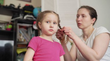 Annem evde küçük bir kızın saçını örüyor. Bir kadın, sabahları küçük kızının saçında saç stili yapar..