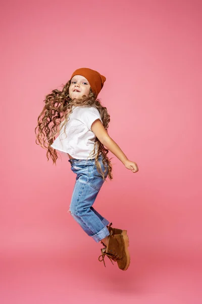 穿着时髦服装 一头卷曲的头发 快乐而时尚的6岁女孩 满身飘飘然 与粉色背景隔离 动态的情感形象 飞在空中 复制空间 — 图库照片