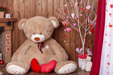 beautiful backdrop for a Valentine's Day photo shoot with a huge teddy bear, a wooden fireplace with candles and flowers, and a tree with red and pink hearts. Romantic mood for the holiday of lovers.