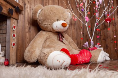 beautiful backdrop for a Valentine's Day photo shoot with a huge teddy bear, a wooden fireplace with candles and flowers, and a tree with red and pink hearts. Romantic mood for the holiday of lovers.