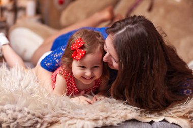 Happy mom and adorable daughter, play, cuddle, laugh and have fun together. A parent and a little girl snuggle up to each other while lying on the floor on a soft fur carpet.