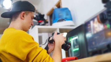 Genç fotoğrafçı, videograf, kameralar, evde fotoğraflar ve videolar. Genç adam fotoğraf ve videoları inceliyor. Program düzenleyicisinde. Serbest çalışan biri. Uzaktan kumanda. Eğitim yeniden başlatılıyor