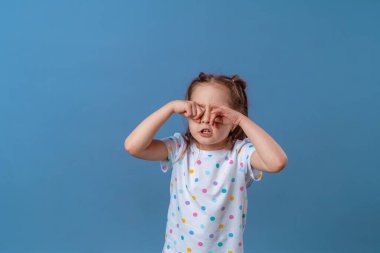 Küçük kız mor bir arka planda elleriyle gözlerini kapatıyor. Bebek yorgun, ağlıyor ve elleriyle gözlerini ovuşturuyor. Boşluğu kopyala.