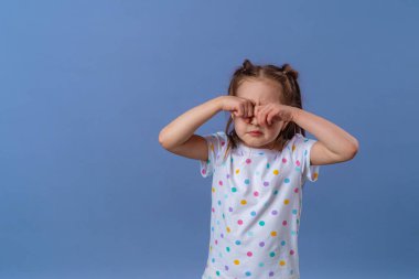 Küçük kız mor bir arka planda elleriyle gözlerini kapatıyor. Bebek yorgun, ağlıyor ve elleriyle gözlerini ovuşturuyor. Boşluğu kopyala.