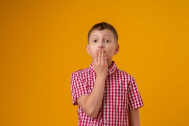 Ağzını eliyle kapatan şaşkın çocuk sarı arka planda duruyor. Çocuk konuşmak istemiyor, bir sır öğrendi. Konuşmadaki sorun. Konuşma gelişimi gecikti. Küfür..