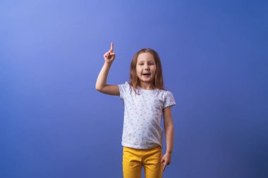 Güzel küçük kız işaret ediyor, mesaj için mekanı gösteriyor. Puantiyeli tişört giymiş gülümseyen, şaşırmış bir çocuk bir şey gösteriyor. Reklam kavramı.