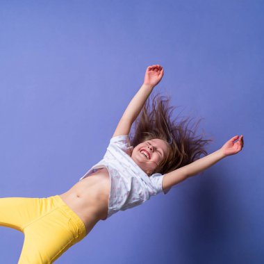 Çılgın heyecanlı küçük kız, mutlu bir şekilde elleri yukarıda, izole edilmiş mor stüdyo arka planında asılı duruyor. Dinamik çocukların imajı. Duygular, ifade. Boşluğu kopyala