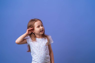 Çekici küçük kız elini kulağına koyup gülümserken mor bir arka planda söylentiler ya da dedikodular duyuyor. Çocuk kulak misafiri ya da işitme zorluğu çekiyor.