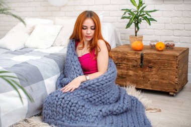 Kızıl saçlı çekici bir kadının portresi, yatağın yanında oturan, büyük örülmüş merino yününden gri bir battaniyeye sarılı. Sonbahar havası, yalıtım