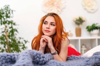 Yatağın üzerinde, büyük örülmüş merino yününden yapılmış gri bir battaniyeye uzanmış kızıl saçlı çekici bir kadının yakın plan portresi. Şehvet ve kadınsı güzellik kavramı..