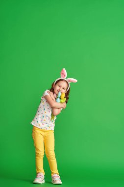 Paskalya tavşanı kulakları ve yeşil arka planda yetişmiş kumaştan yapılma bir buket bahar lale çiçeğiyle mutlu bir kız. Çocuk bahar ve Paskalya geldiğinde gülümser ve sevinir..