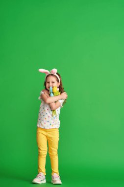 Paskalya tavşanı kulakları ve yeşil arka planda yetişmiş kumaştan yapılma bir buket bahar lale çiçeğiyle mutlu bir kız. Çocuk bahar ve Paskalya geldiğinde gülümser ve sevinir..