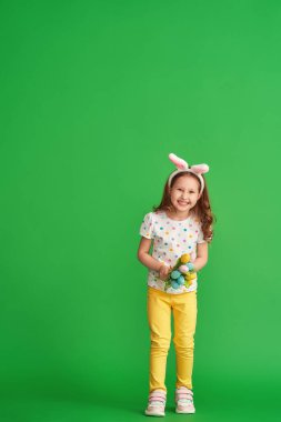 Paskalya tavşanı kulakları ve yeşil arka planda yetişmiş kumaştan yapılma bir buket bahar lale çiçeğiyle mutlu bir kız. Çocuk bahar ve Paskalya geldiğinde gülümser ve sevinir..