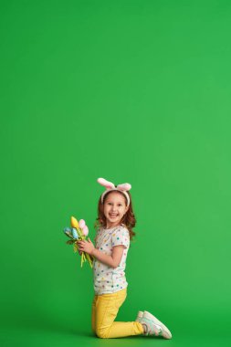 Paskalya tavşanı kulakları ve yeşil arka planda yetişmiş kumaştan yapılma bir buket bahar lale çiçeğiyle mutlu bir kız. Çocuk bahar ve Paskalya geldiğinde gülümser ve sevinir..