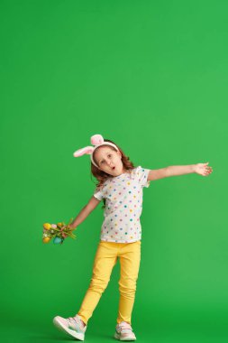 Paskalya tavşanı kulaklı ve çiçek desenli lale çiçekli küçük bir kız yeşil arka planda dans edip kumaş yapmış. Çocuk bahar ve Paskalya geldiğinde gülümser ve sevinir..