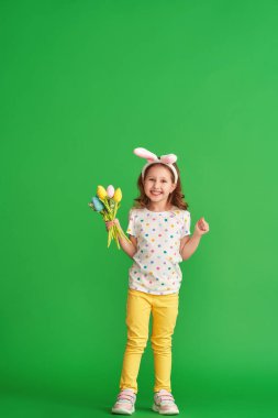 Paskalya tavşanı kulakları ve yeşil arka planda yetişmiş kumaştan yapılma bir buket bahar lale çiçeğiyle mutlu bir kız. Çocuk bahar ve Paskalya geldiğinde gülümser ve sevinir..