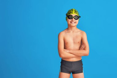 Mavi arka planda, mayo, gözlük ve mayo takan sportif bir çocuğun portresi. Çocuk bir spor okulunda spor yapmaktan mutlu. Sağlıklı yaşam tarzı ve spor kavramı.