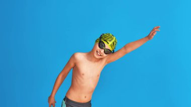 Mayolu, gözlüklü ve mayo giymiş mavi arka planda egzersiz yapan bir çocuğun portresi. Çocuk spor okulunda yüzmekten hoşlanıyor. konsept sağlıklı yaşam tarzı ve spor.