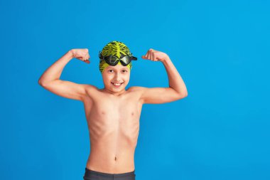 Mayolu, gözlüklü ve mayo giymiş mavi arka planda kaslarını gösteren sportif bir çocuğun portresi. Çocuk bir spor okulunda yüzmekten hoşlanıyor. konsept sağlıklı yaşam tarzı ve spor