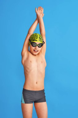 Mayolu, gözlüklü ve mayo giymiş mavi arka planda egzersiz yapan bir çocuğun portresi. Çocuk spor okulunda yüzmekten hoşlanıyor. konsept sağlıklı yaşam tarzı ve spor.