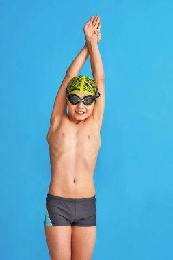 Mayolu, gözlüklü ve mayo giymiş mavi arka planda egzersiz yapan bir çocuğun portresi. Çocuk spor okulunda yüzmekten hoşlanıyor. konsept sağlıklı yaşam tarzı ve spor.