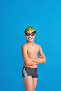 Mavi arka planda, mayo, gözlük ve mayo takan sportif bir çocuğun portresi. Çocuk bir spor okulunda spor yapmaktan mutlu. Sağlıklı yaşam tarzı ve spor kavramı.