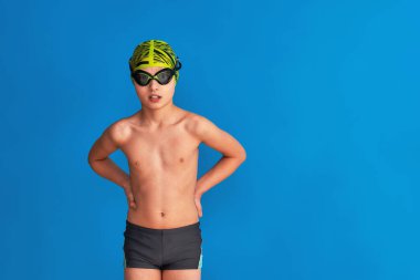 Mavi arka planda, mayo, gözlük ve mayo takan sportif bir çocuğun portresi. Çocuk bir spor okulunda spor yapmaktan mutlu. Sağlıklı yaşam tarzı ve spor kavramı.