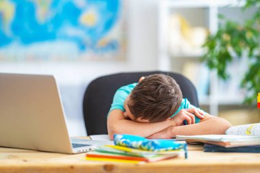 üzgün küçük bir çocuk, bir okul çocuğu, evde çalışmak için dizüstü bilgisayar kullanıyor. Çocuk öğrenmekten sıkılır ve uzaktan bilgi kazanır. Öğrenci okula gitmek istiyor. Dijital e-öğrenme kavramı. Uzak.