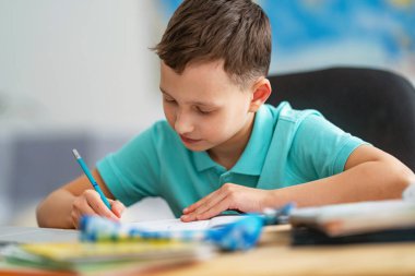 Küçük çocuk masasında oturuyor, ev ödevini yapıyor. Çocuk mutlu bir şekilde gülümsüyor ve karantina döneminde bilgi kazanıyor. dijital konsept e-öğrenme, salgın sırasında, kendini izole etme.