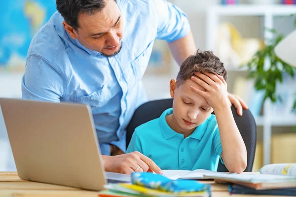 caring father helps his son with homework, using a laptop during distance learning. A parent explains a new topic to a child in an online lesson. Achieving perfection together. Problems with learning
